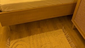 Una cama individual con estructura de madera, ropa de cama blanca y una toalla enrollada al lado.