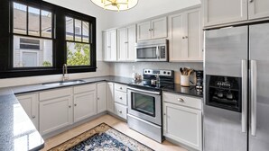 A modern kitchen with white cabinets, stainless steel appliances, a large window, and a chandelier.