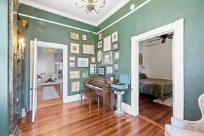 Une pièce avec un piano, un banc, une table sur laquelle se trouve un objet bleu, et un lit.