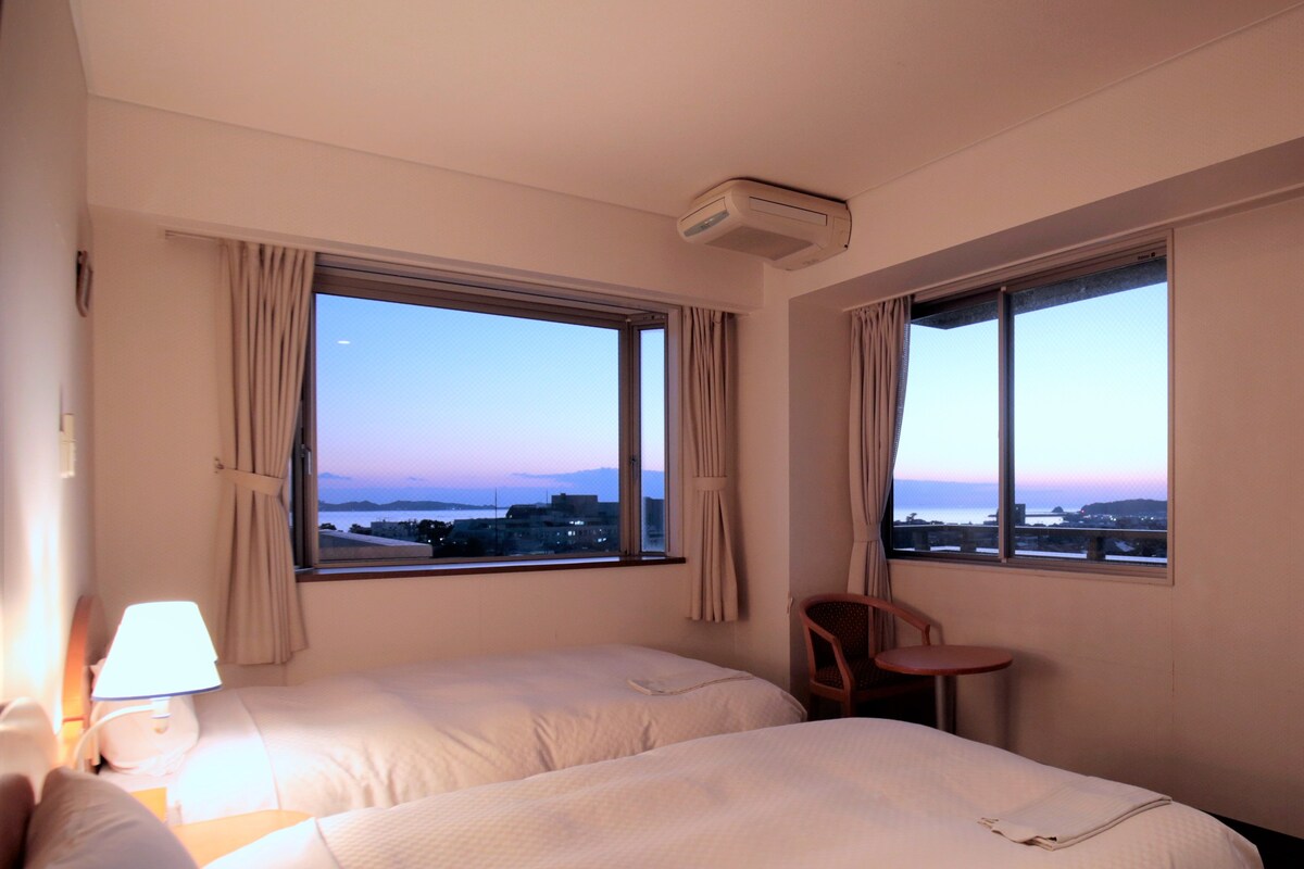 Habitación de hotel con dos camas, una silla, una mesa y una lámpara.