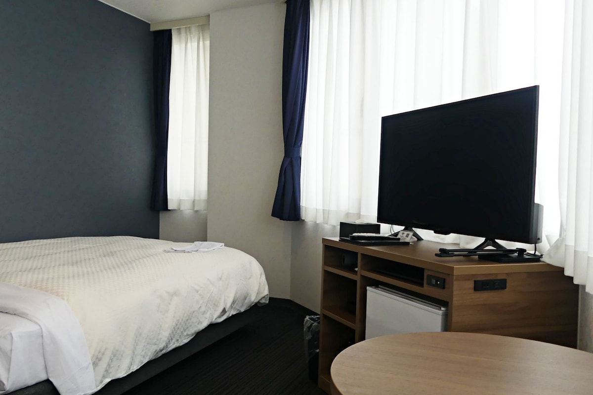 A hotel room with a bed, a desk with a computer, a TV, and a small table.