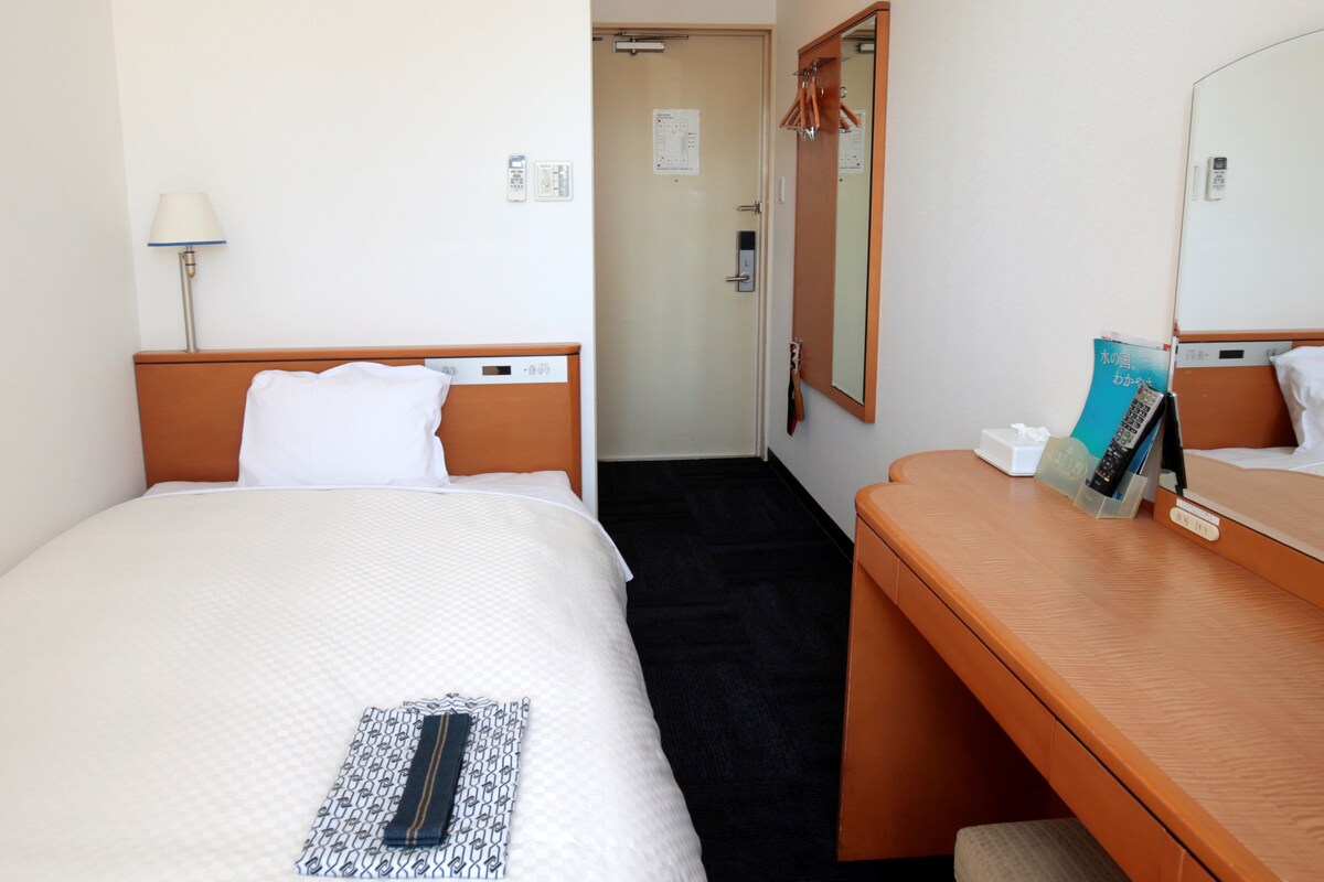 Una habitación de hotel con cama, mesita de noche y espejo.