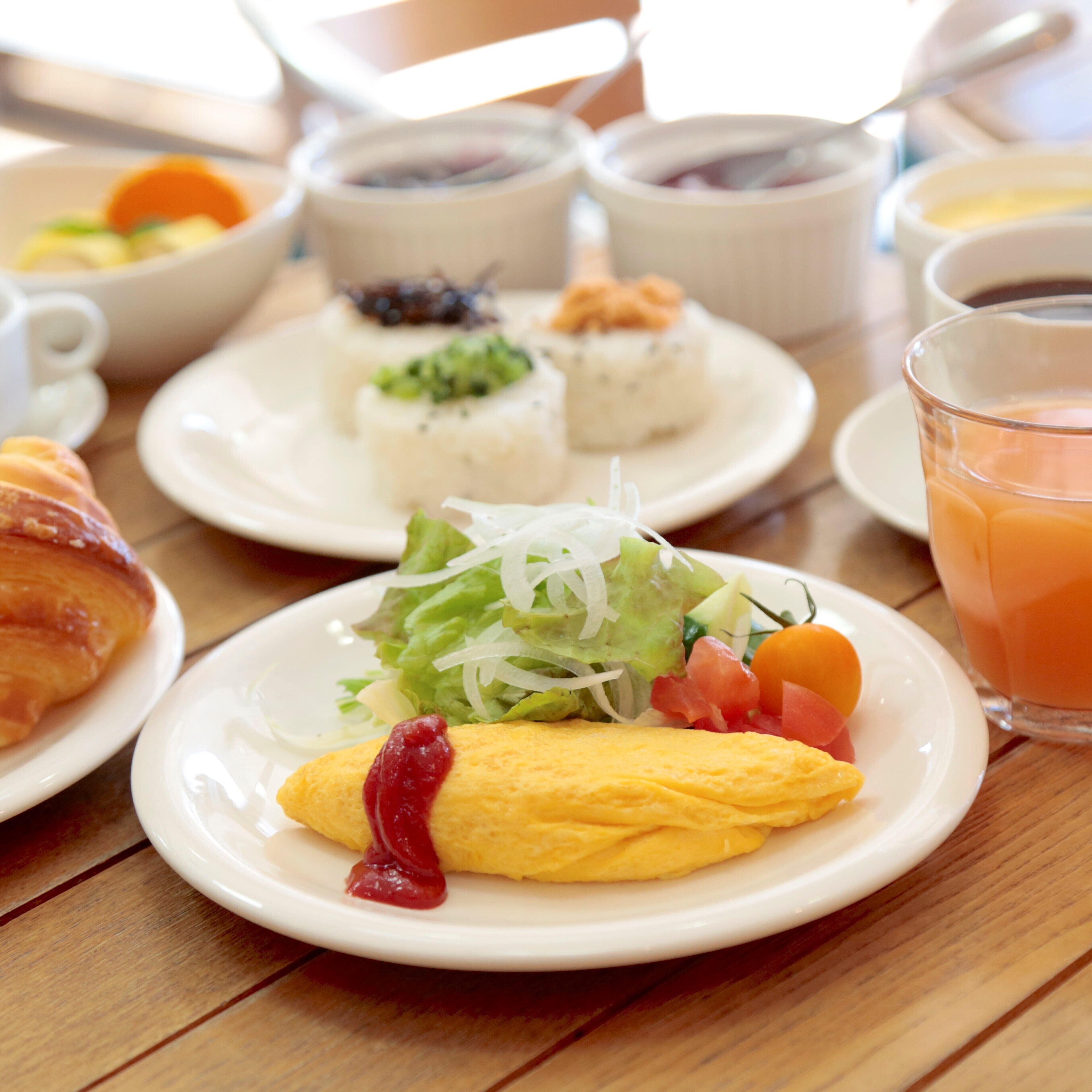 A breakfast setting with various dishes including an omelette, salad, and fruit on a wooden table.