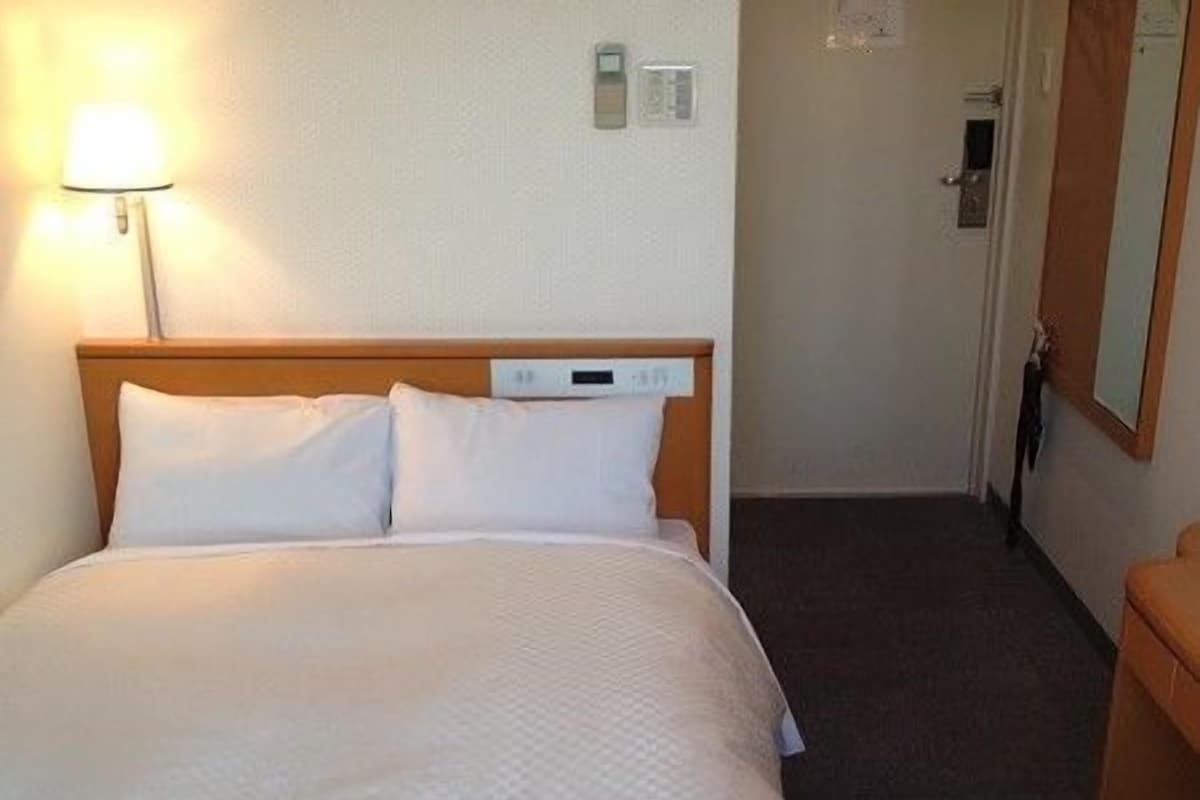 A hotel room with a neatly made bed, a bedside lamp, and a door leading to another room.