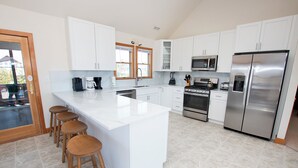 Een moderne keuken met witte kasten, een roestvrijstalen koelkast, een koffiezetapparaat en een groot kookeiland met barkrukken.