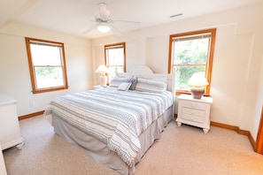 Ein Schlafzimmer mit Bett, Nachttischen, Deckenventilator und Fenstern.
