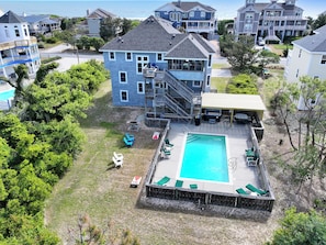 Ein zweistöckiges Haus mit Swimmingpool, Sitzgelegenheiten im Freien und einer überdachten Terrasse.