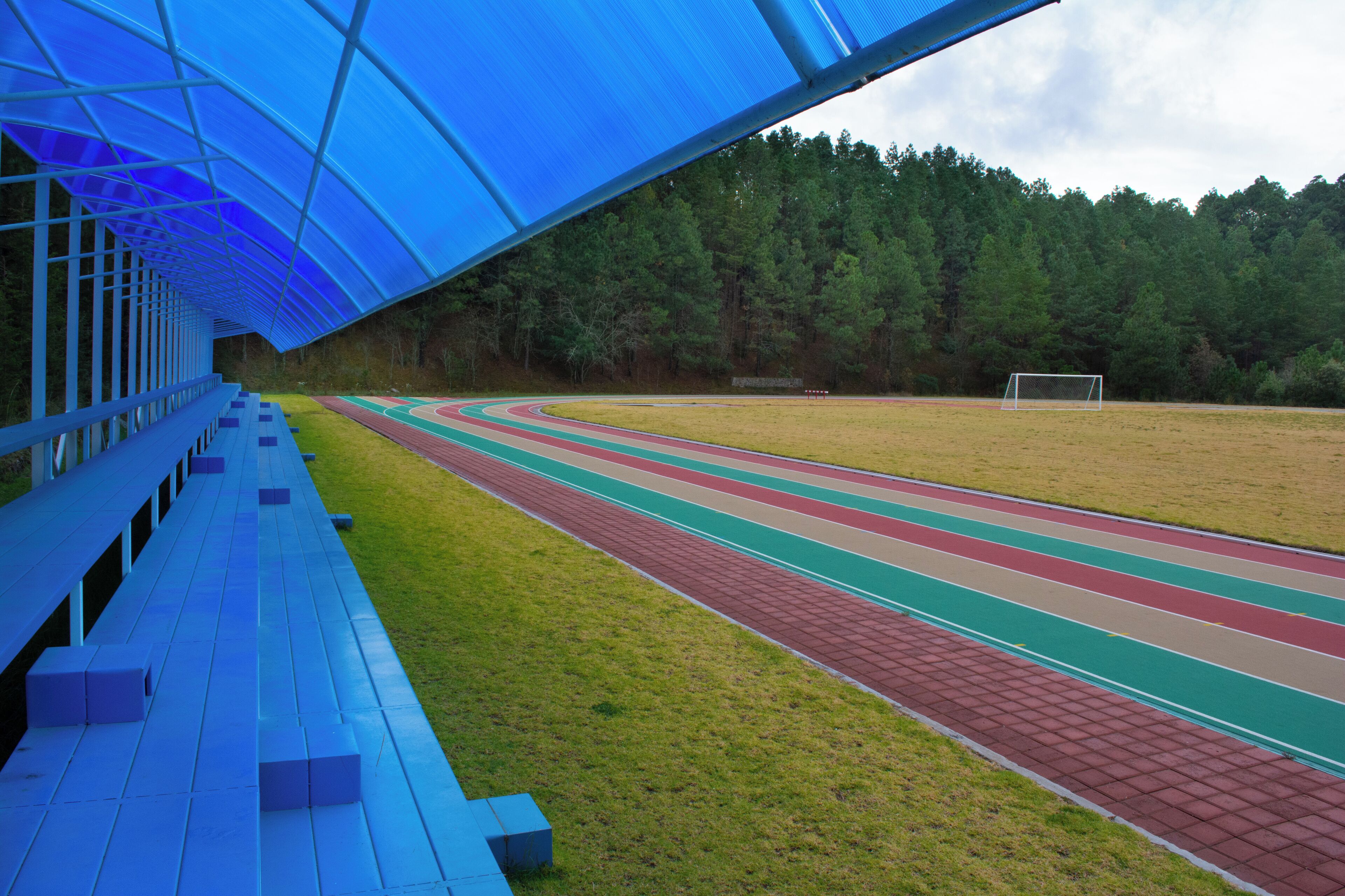 A running track with a blue roof structure, a green field, and a goal post.