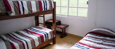 Habitación con literas, vista al exterior por una ventana, una pequeña mesa de madera y ropa de cama a rayas.