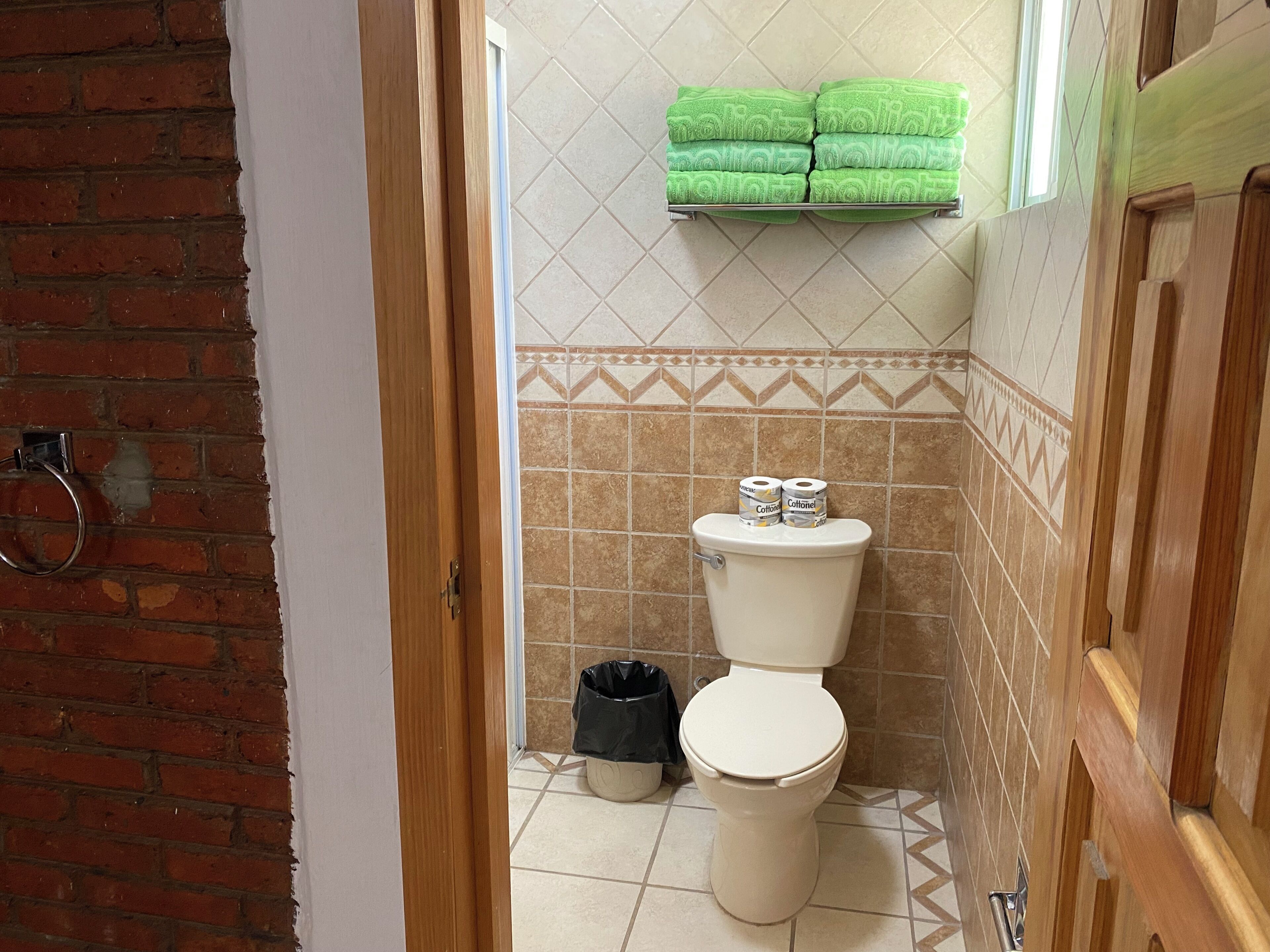 Ein Badezimmer mit Toilette, Mülleimer und Ablagefläche mit grünen Handtüchern.