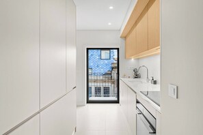 Eine moderne Küche mit weißen Schränken, einem eingebauten Backofen und einem Fenster mit Blick auf einen balkonartigen, blau gekachelten Bereich.