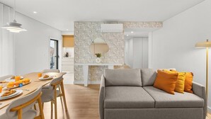 A modern living room with a grey sofa, orange cushions, a dining area with wooden chairs, and a kitchen in the background. - Urban Comfort @ Bonfim Boutique Flats (Porto)