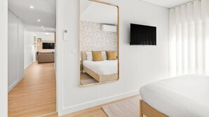 A bedroom with a bed, a large mirror, a television, and a view into the adjacent living area. - Urban Comfort @ Bonfim Boutique Flats (Porto)