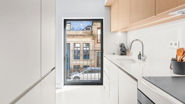 A modern kitchen with white cabinets, a black countertop, and a view of a building through a glass door. - Urban Comfort @ Bonfim Boutique Flats (Porto)