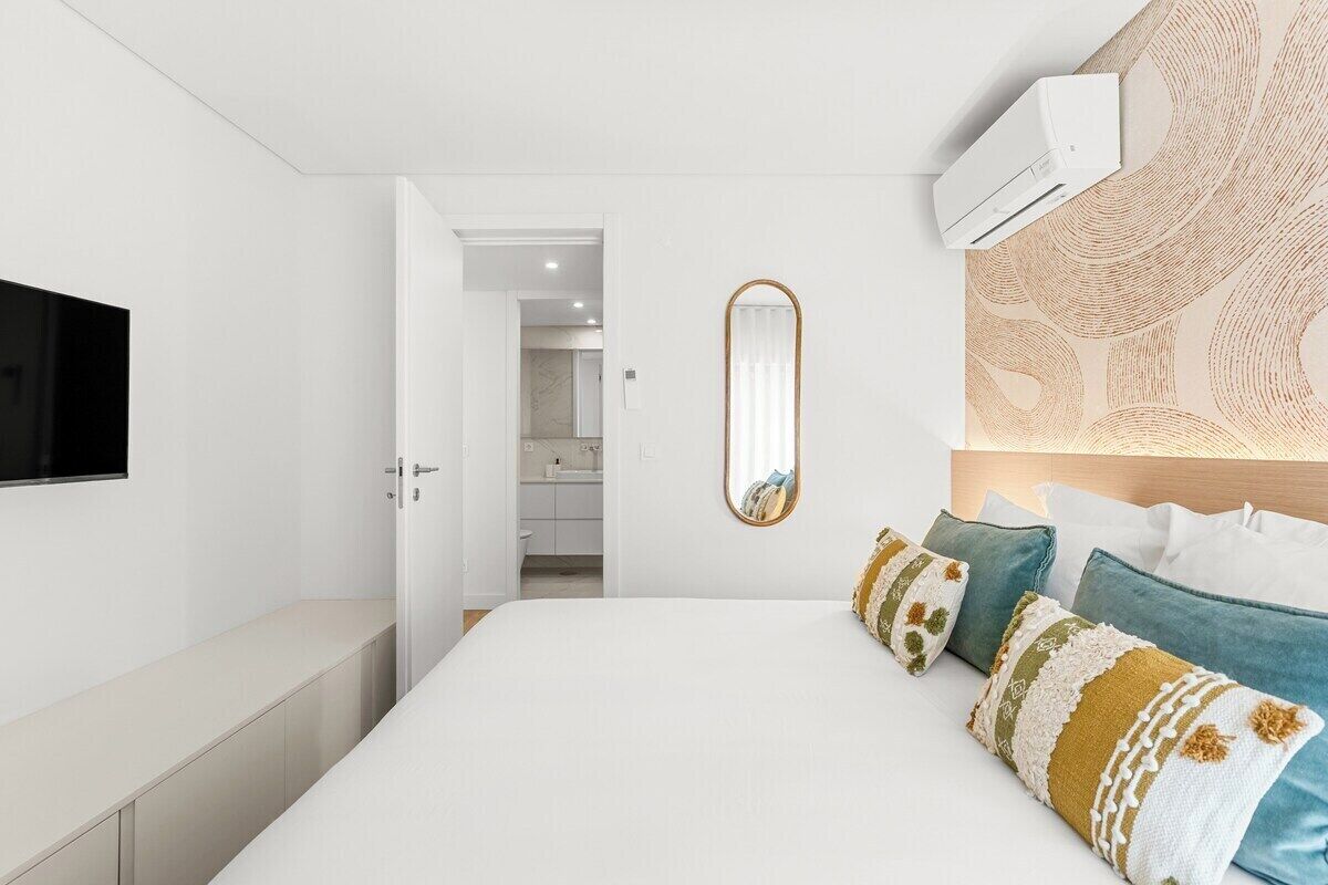 A bedroom with a bed, bedside table, wall-mounted TV, and a mirror.