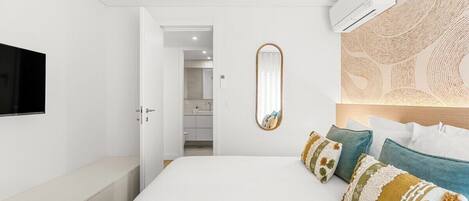 A bedroom with a bed, bedside table, wall-mounted TV, and a mirror.
