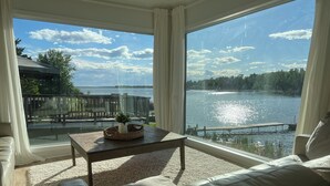 Un salon moderne doté d’une grande fenêtre donnant sur un lac, d’une terrasse en bois et d’une vue imprenable sur l’eau.