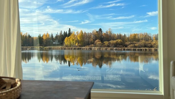 Une pièce dotée d’une grande fenêtre donnant sur un lac et des arbres aux couleurs automnales.