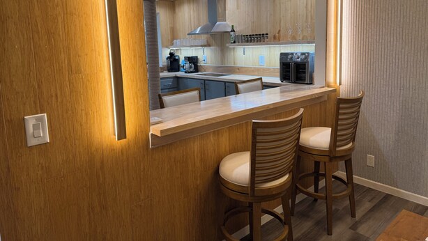 Une cuisine moderne avec des meubles en bois, un four encastré et un coin bar équipé de deux tabourets.