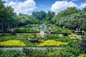 A garden with a central fountain, surrounded by neatly trimmed hedges and various flowering plants. - Downtown ATL High-Rise | Kings, Views & Pool (Atlanta)