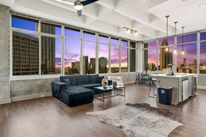 A spacious living room with a large window offering a city view, a modern kitchen, and a cozy seating area. - Downtown ATL High-Rise | Kings, Views & Pool (Atlanta)