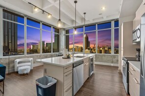 Una cocina moderna con una isla grande, lavavajillas integrado y vistas a un horizonte urbano al atardecer.