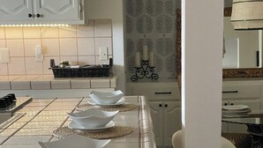 Una cocina con una mesa larga dispuesta con cuencos blancos y posavasos, una lámpara colgante y una pared con diseño.