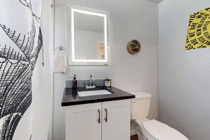 A bathroom with a black countertop sink, a white toilet, and a mirror with a light. There is a towel rack and a small plant on the wall. - No.7: King bed, 1bd/1ba, UNM (Albuquerque)