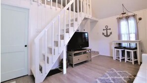 Een kamer met een witte trap, een televisie op een houten standaard, een witte deur en een muur met een ankerdecoratie.