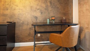 Un espace de bureau moderne avec un plancher en bois, un bureau noir, un fauteuil en cuir marron et un mur à texture.