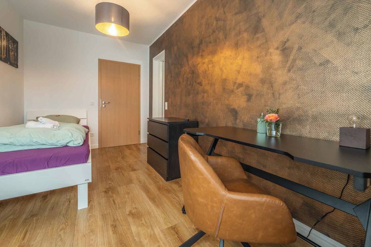 A compact room with a bed, a desk, a chair, and a textured wall.