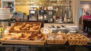Un espace buffet proposant une variété d’aliments, notamment du pain, des viennoiseries et des œufs, ainsi que des machines à café et de la vaisselle.