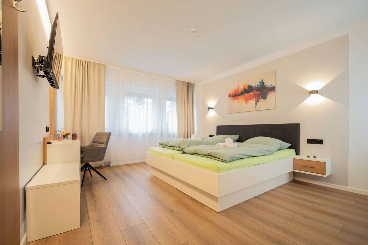 A modern bedroom with a bed, a chair, a desk, and a painting on the wall.