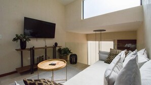 Ein modernes Wohnzimmer mit großem Fernseher, einer Couch, einem Couchtisch und einer Pflanze.