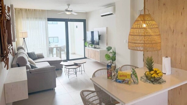Un salon moderne avec un canapé, une table à manger et des chaises. Un téléviseur est fixé au mur et un ventilateur de plafond est installé.