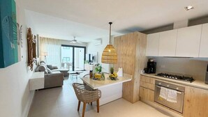 Une cuisine moderne dotée d’un îlot central, d’un coin repas avec des chaises et d’un espace de vie comprenant un canapé et un ventilateur de plafond.