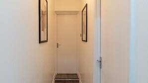 A narrow hallway with wooden flooring, white walls, and two framed pictures on the left wall. - Modern Flat in Waterloo (London)