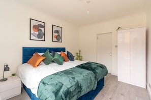 A bedroom with a bed, white nightstands, a wardrobe, and two abstract paintings on the wall. - Modern Flat in Waterloo (London)