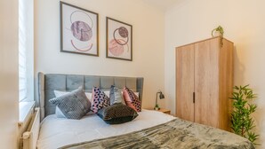 A neatly made bed with patterned pillows, a grey headboard, and a large wardrobe. - Modern Flat in Waterloo (London)