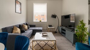 A modern living room with a grey sofa, a coffee table, a TV, and a small side table. - Modern Flat in Waterloo (London)