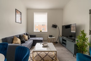 A modern living room with a grey sofa, a coffee table, a TV, and a small side table. - Modern Flat in Waterloo (London)
