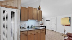 Une cuisine avec des meubles de rangement en bois, un évier et un plan de travail. On y trouve une porte avec une fenêtre, une lampe et une chaise.