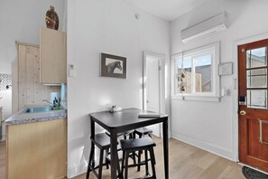 A kitchen with a wooden cabinet, a sink, and a table with two stools. There is a framed picture on the wall and a door with a window.