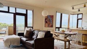 Un salon moderne avec un canapé en cuir, une table à manger et un coin cuisine doté de grandes fenêtres.