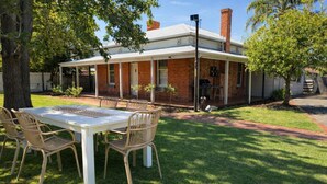 A brick house with a covered porch, a dining table with chairs, and a barbecue grill.