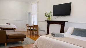 A hotel room with a bed, a chair, a small table, a TV, and a window with blinds.