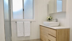 A modern bathroom with a glass shower enclosure, a white sink, and wooden cabinetry.