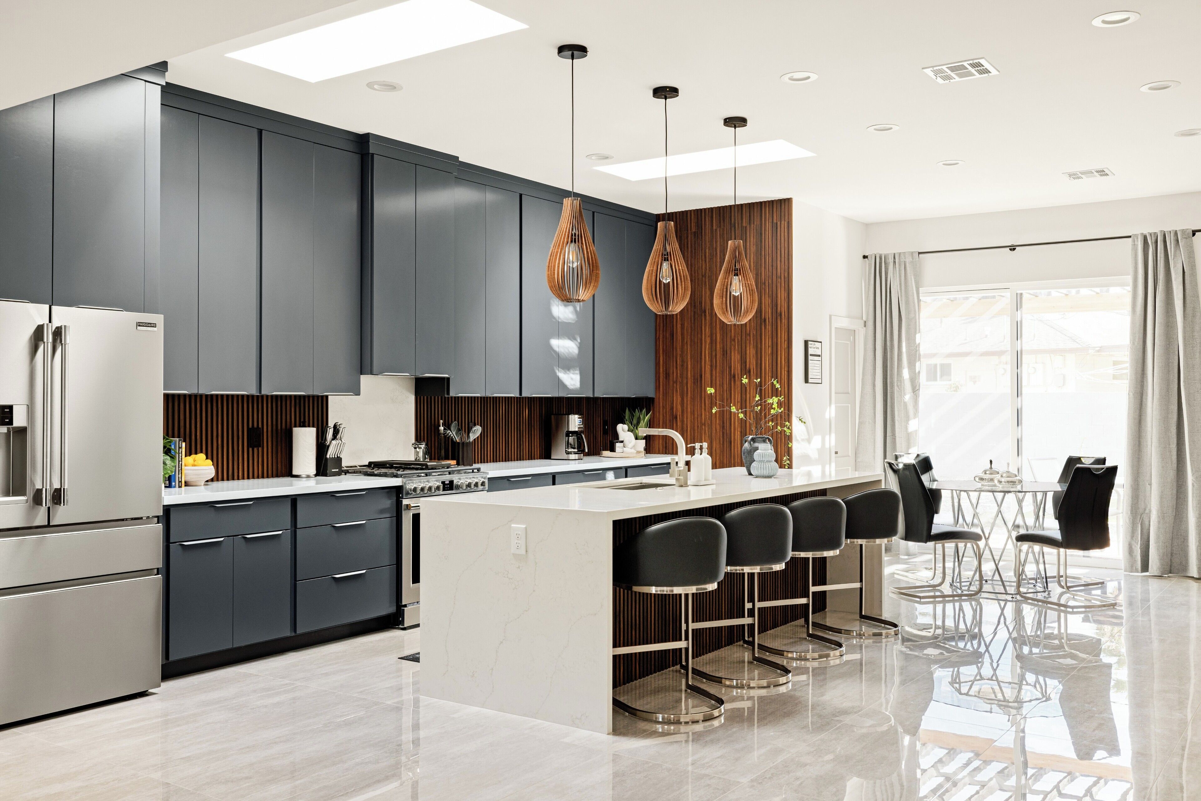 Una cocina moderna con armarios oscuros, una isla central con taburetes de bar e iluminación colgante.
