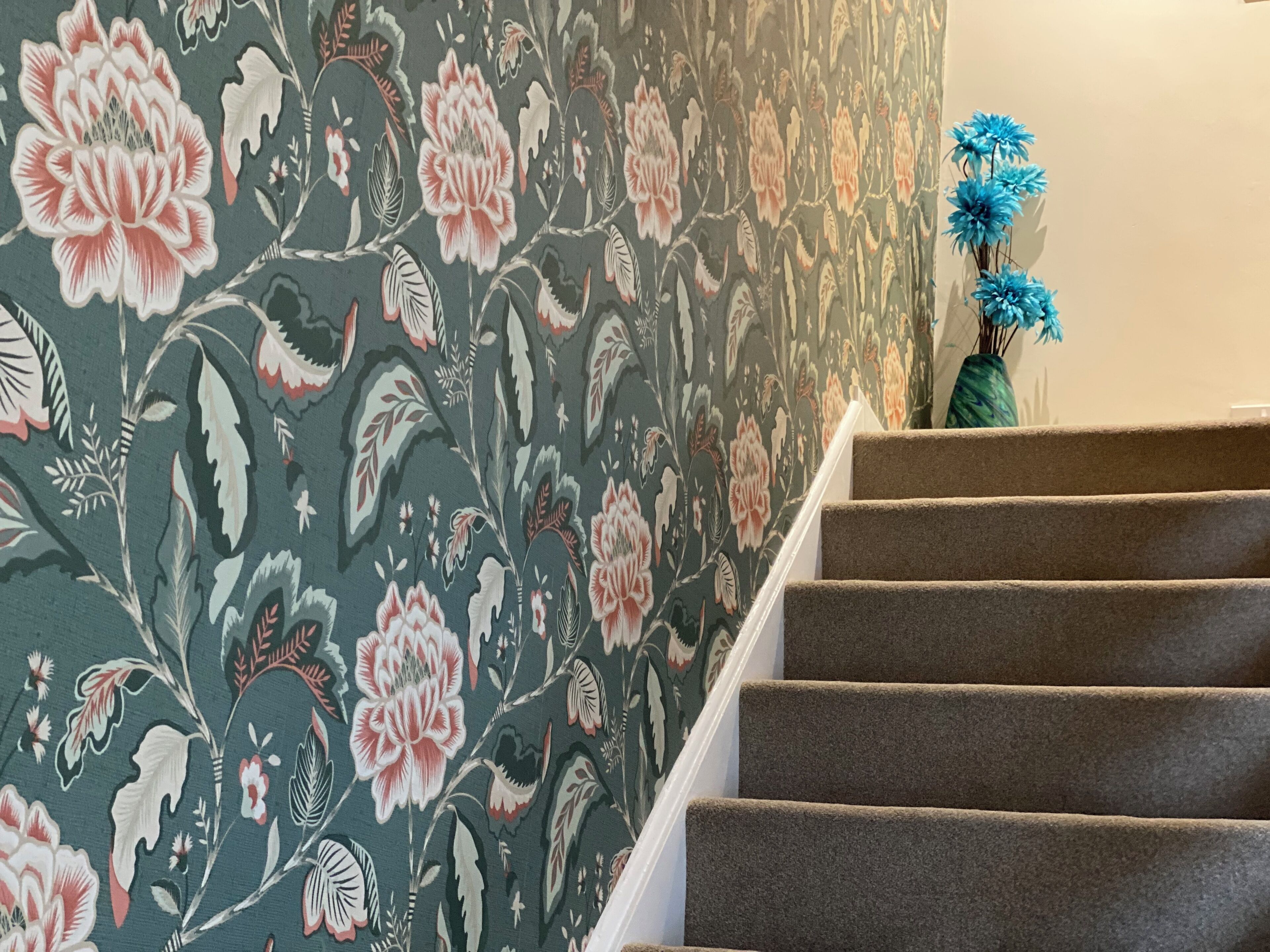 A staircase with carpeted steps and a floral wallpaper pattern.