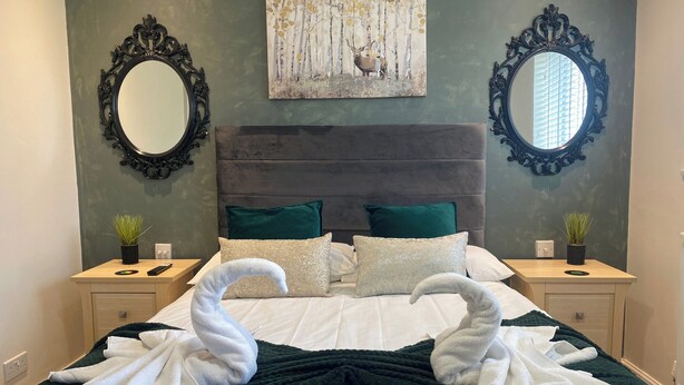 A neatly made bed with two towels shaped like swans, a dark green throw blanket, and two decorative pillows. - Cozy Bedford Home with 3 Bedrooms (Bedford)